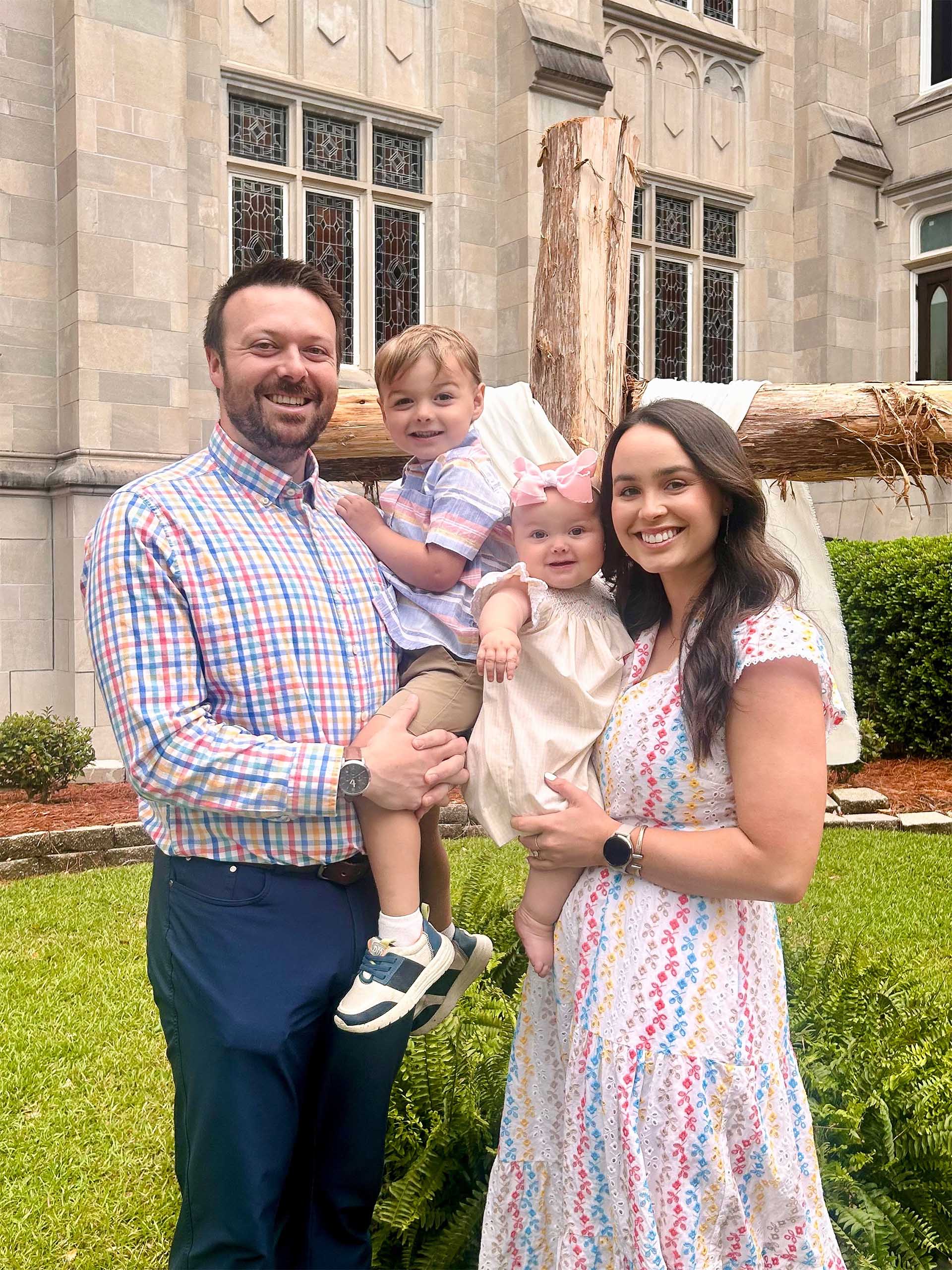 Photo of large family with grandmother, adult children, and grandchildren in front of cross at First Baptist Jackson. One child is holding a puppy.