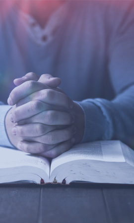 Photograph of praying hands on an open Bible